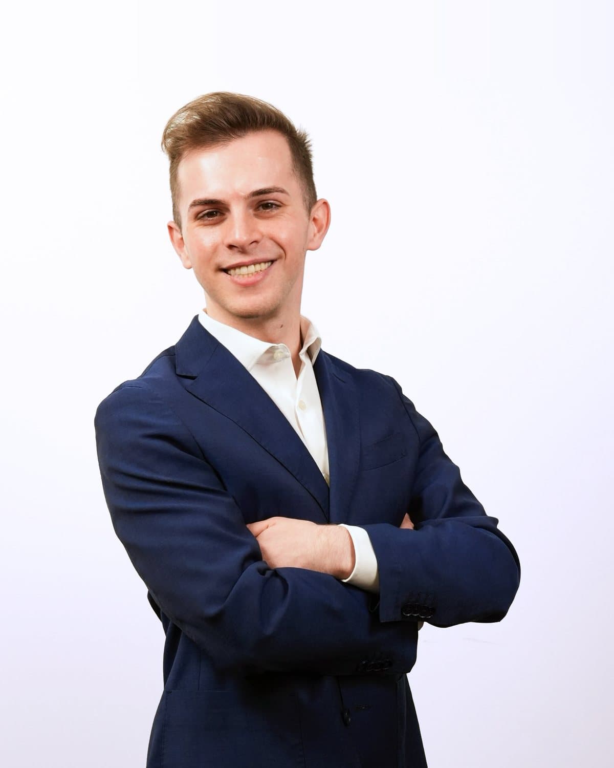 Elijah Pallay, smiling, arms crossed, in a navy suit jacket and white shirt
